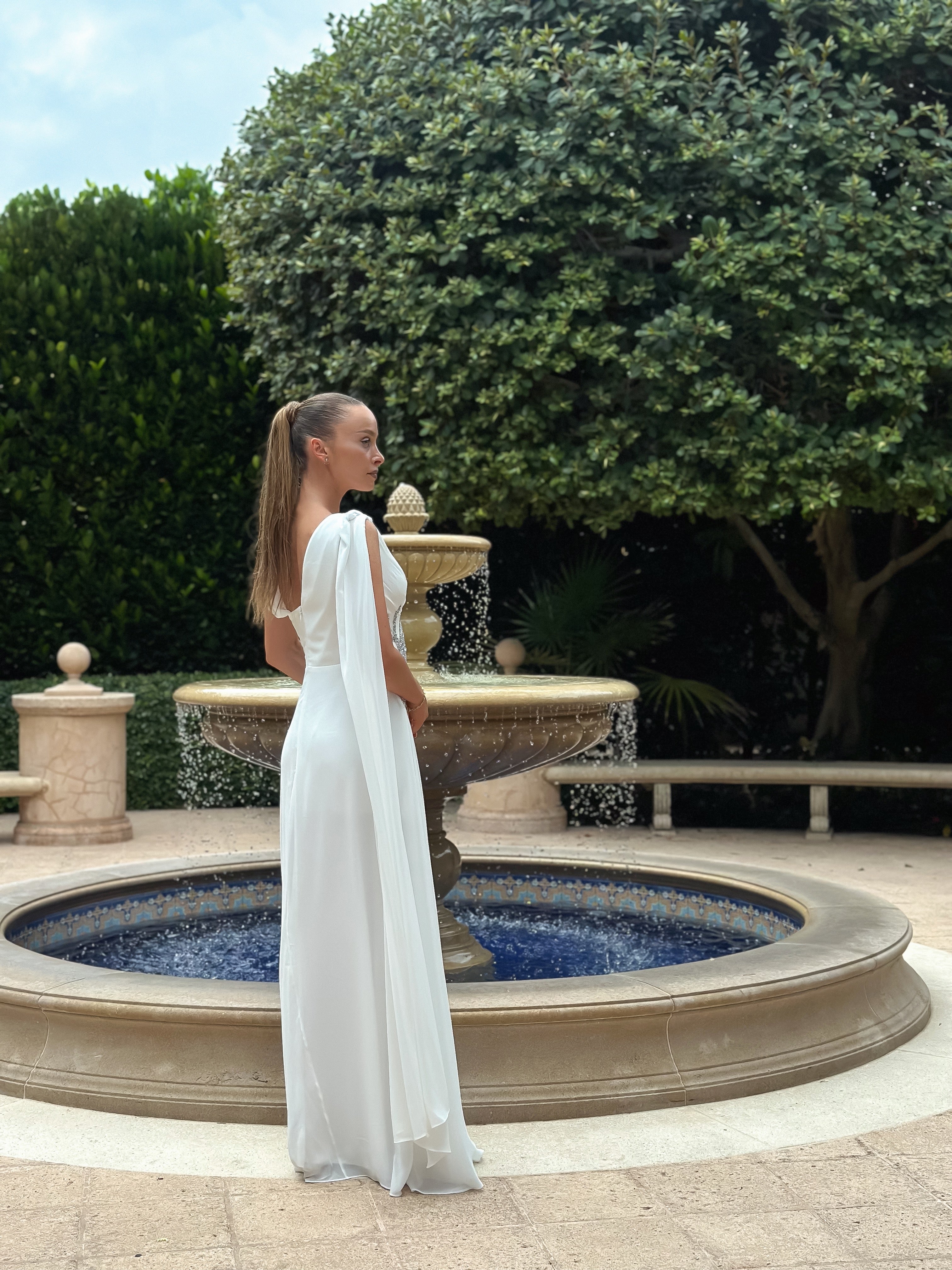 "White Serenade" flowing white gown with draped bodice, silver waist embellishment, and subtle slit, perfect for weddings, galas, or formal events, exuding timeless elegance and sophistication.