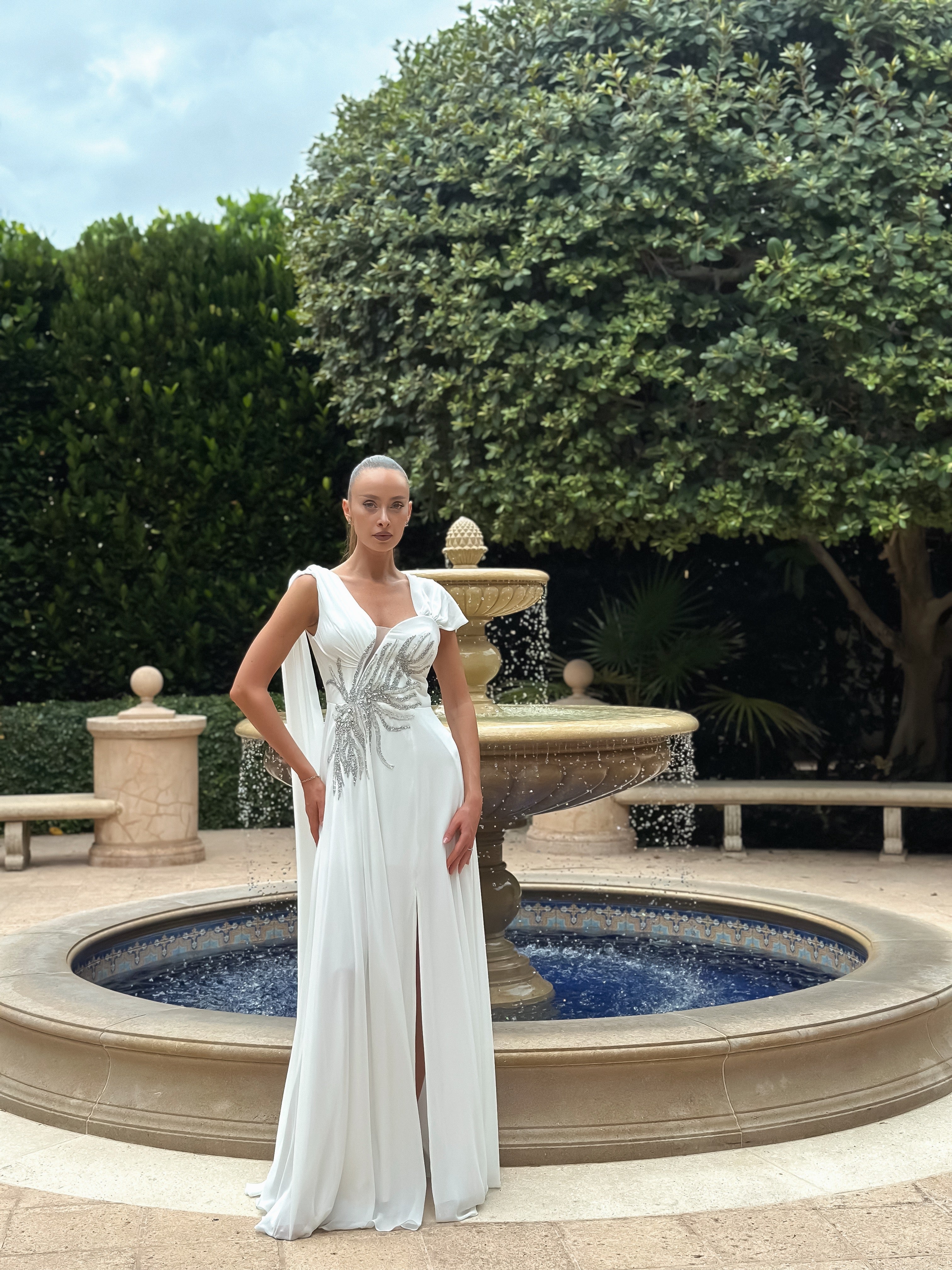 "White Serenade" flowing white gown with draped bodice, silver waist embellishment, and subtle slit, perfect for weddings, galas, or formal events, exuding timeless elegance and sophistication.